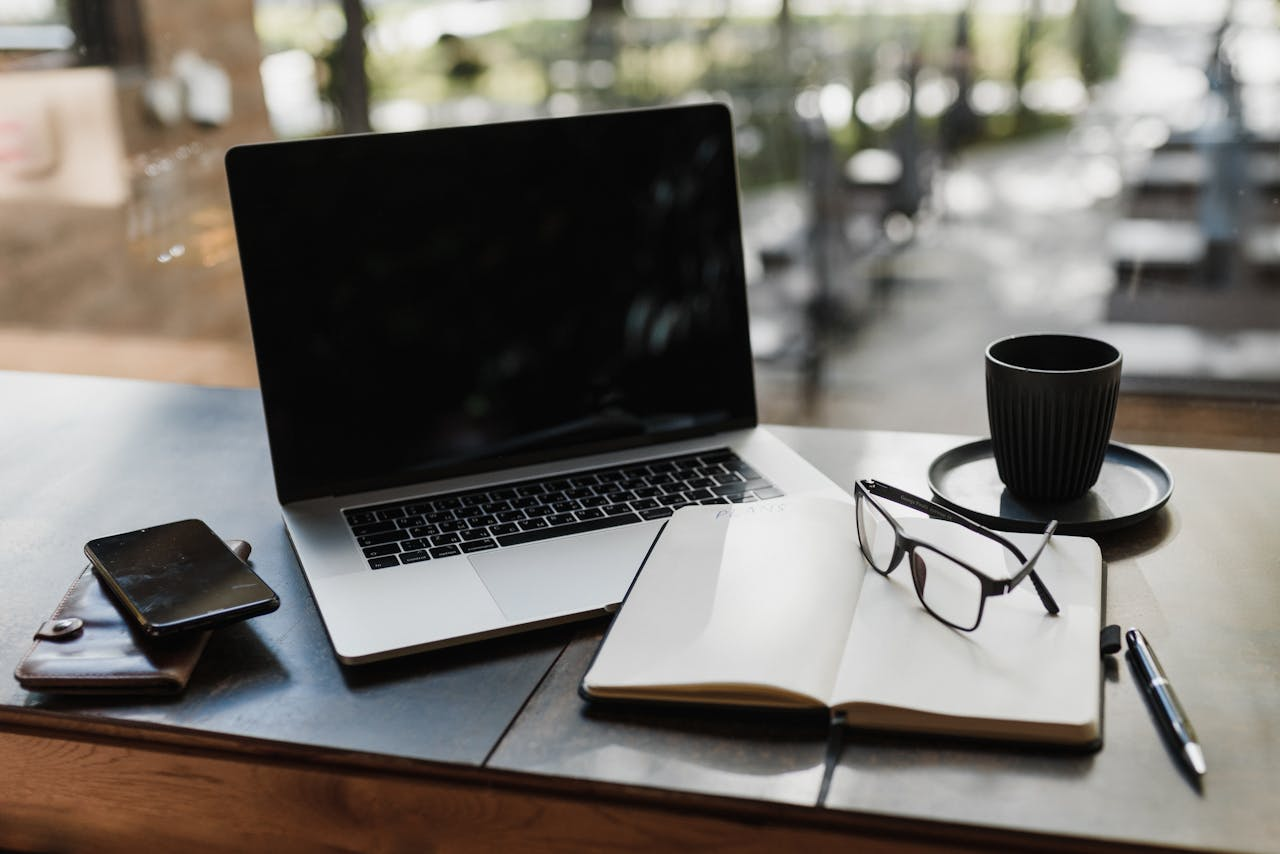 Workspace setup featuring a laptop, notepad, glasses, and coffee cup for productivity.